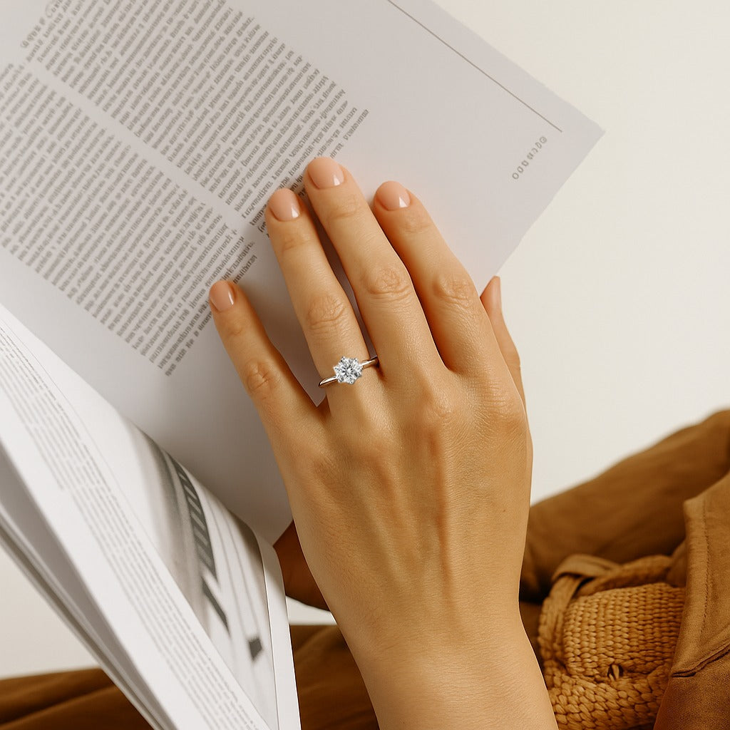 Hand with a ring on an open book, wearing a brown coat.